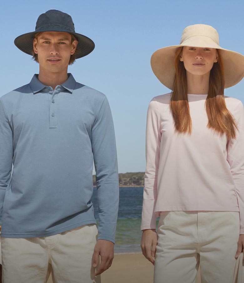 A man and a woman standing on the beach in sun hats.