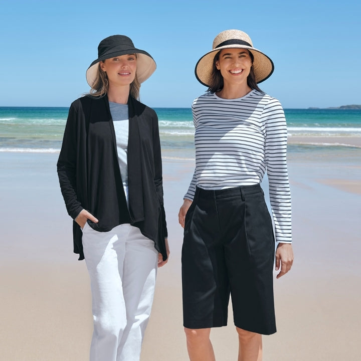 Two women standing on a beach with ocean and sky in the background wearing UPF 50+ Solbari sun hats and sun protective clothing.