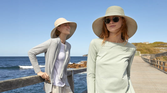 Two women wearing Solbari UPF 50+ sun hats and clothing with the sea and a blue sky behind them
