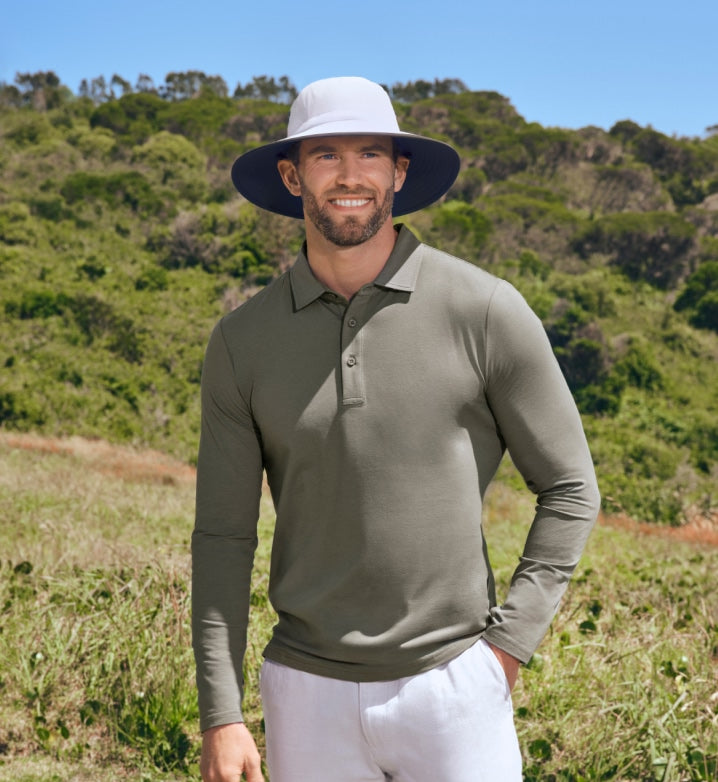 Man wearing a green Solbari long-sleeve polo shirt and white pants standing in a grassy field with a blue sky.