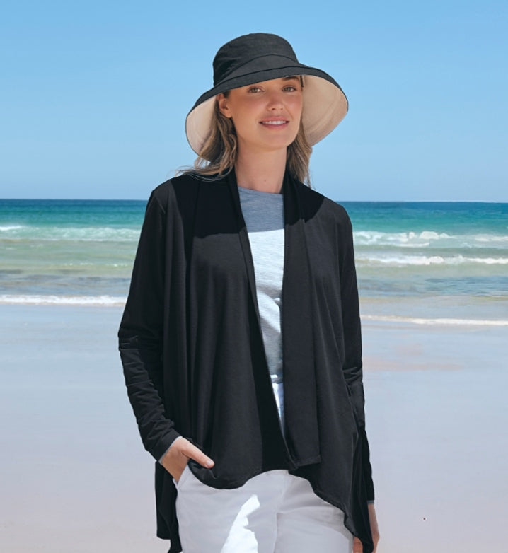 Woman wearing a Solbari UPF 50+ black sun hat and black sun protective cardigan on a beach.