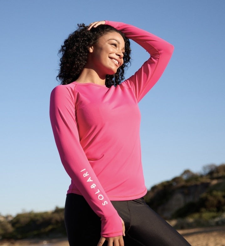 Woman wearing a pink Solbari long-sleeve rash guard with 'SOLBARI' on the arm, on a clear day.