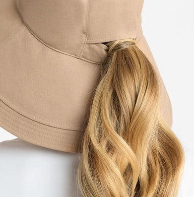Blonde ponytail coming through a ponytail hole in a beige hat on a white background