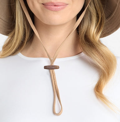 A beige hat with a neck cord worn by a person on a white background