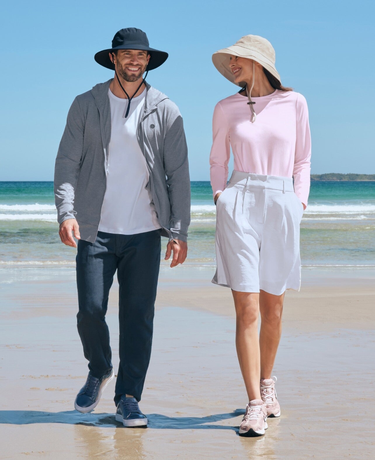 Man and woman walking on a beach wearing Solbari UPF 50+ sun hats and casual sun protective clothing.