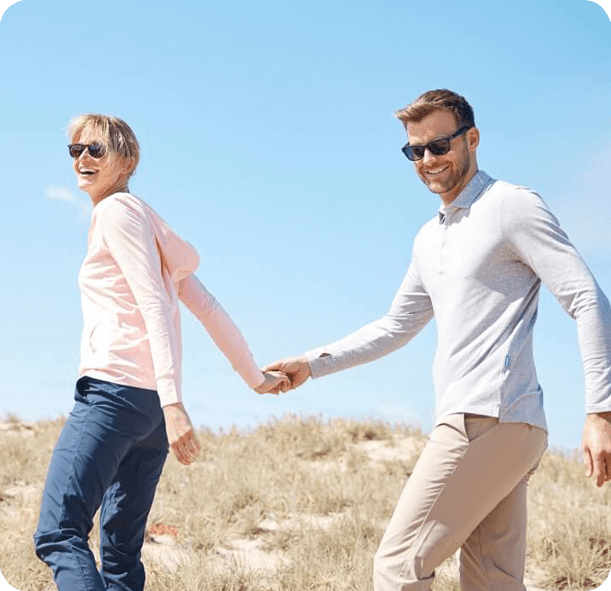 A woman and a man holding hands and walking with a blue sky in the background.